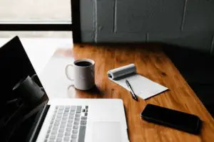 Macbook pro, mug, and black smartphone on table