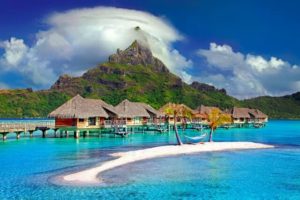 Image of over the water bungalows and a mountain - things to stop buying to save lots of money