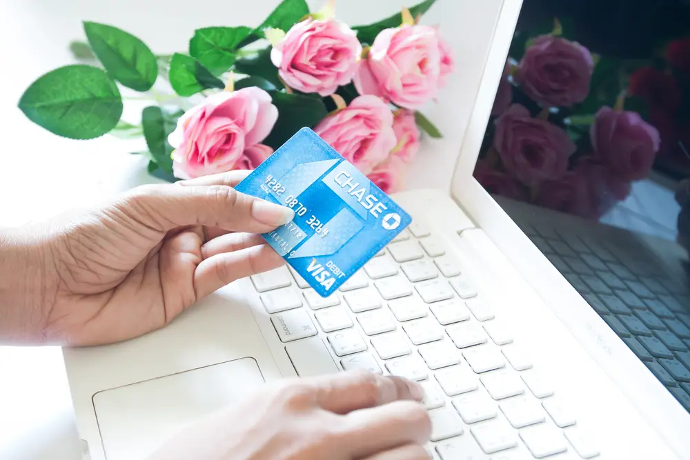 Woman hand holding debit card of Chase Bank and using an Apple MacBook White